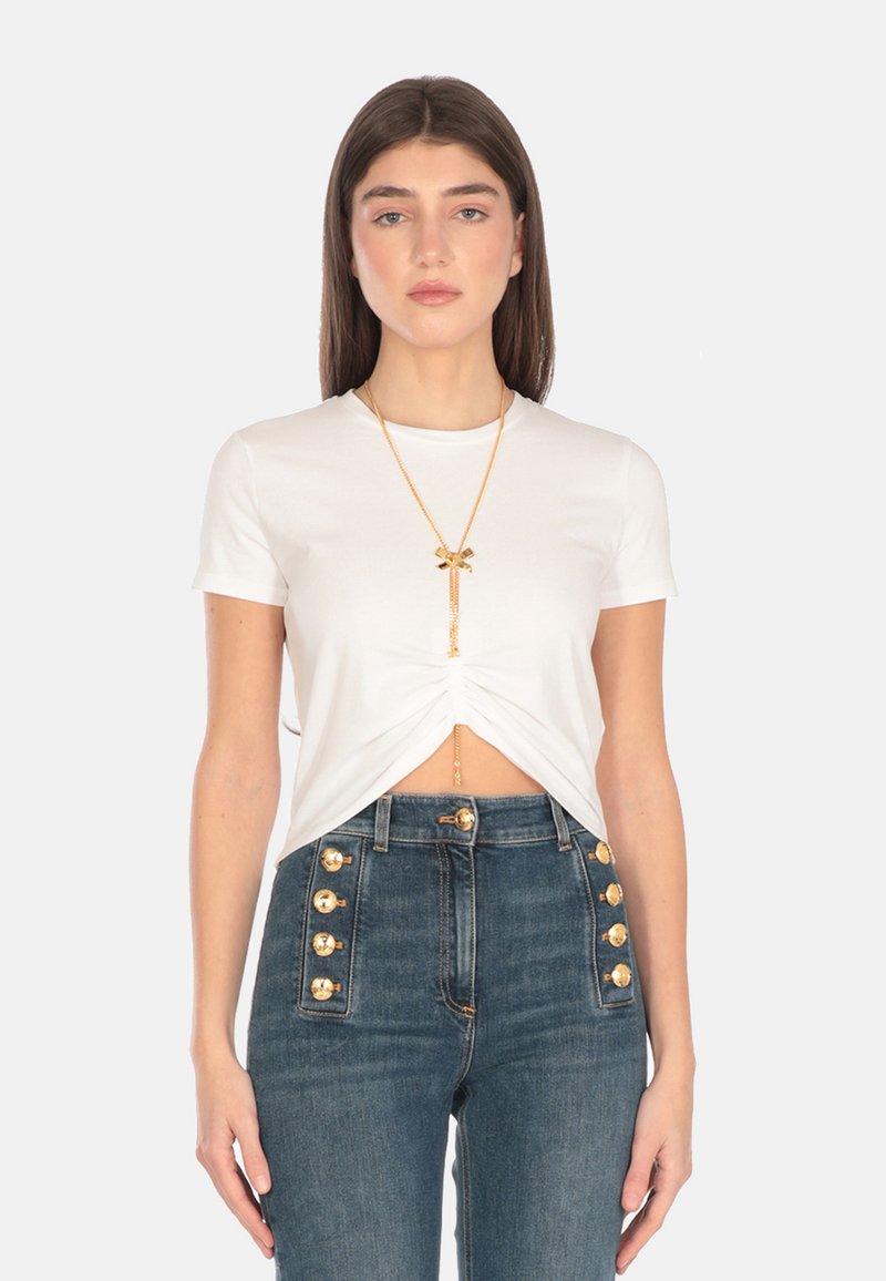 Top bianco a maniche corte con design frontale annodato. Abbinato a jeans in denim a vita alta con dettagli in bottone dorato.