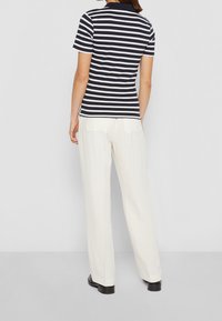 Marlijn en witte gestreepte polo met korte mouwen, gecombineerd met crèmekleurige wijde broeken en zwarte schoenen, gezien vanuit de achterkant.