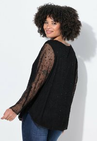 Top in maglia nera trasparente con maniche lunghe, superficie testurizzata e sottili dettagli di perline; abbinato a jeans in denim.