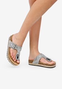 Sandali argento con una cinghia testurizzata, suola in sughero e accenti neri. Suola piatta con un tacco leggermente sollevato per il comfort.