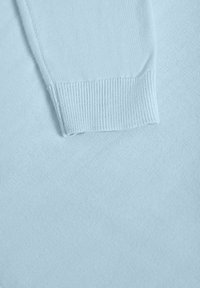 Manche de pull tricoté bleu clair avec poignet côtelé posée sur un fond en tissu assorti.