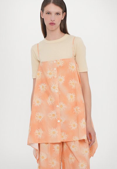 Oranje bloemenprint jurk met spaghettibandjes, met een loose fit en knopen aan de voorkant. Draag een beige strakke top eronder.