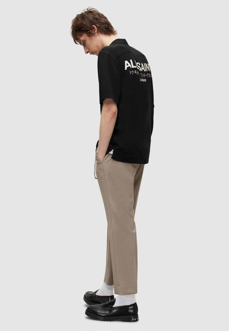 Black short-sleeve shirt with "ALLSAINTS" text on the back, paired with beige pants and black loafers. Socks are white.