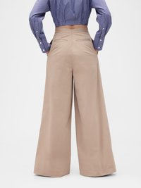 Pantaloni beige a gamba larga con una texture liscia, vita alta e due tasche posteriori. Mostrati di spalle con una camicia corta a righe blu.