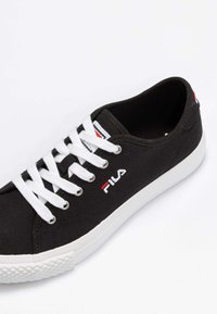 Sneaker nera in tela con lacci bianchi e suola in gomma. Presenta un logo rosso e bianco sul lato e un design con punta arrotondata.