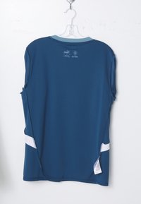 Maillot de sport Puma bleu suspendu, côté dos visible avec col bleu clair, accents latéraux blancs et étiquette d'entretien sur le côté inférieur droit.