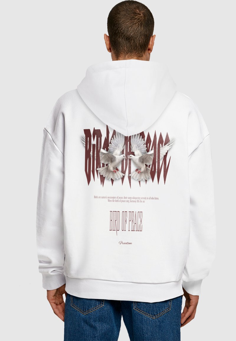 Bílá mikina s kapucí se grafikou dvou holubic a textem "PTÁK MÍRU" a "Svoboda" v tučném, stylizovaném písmu. Měkčená látka, volný střih.