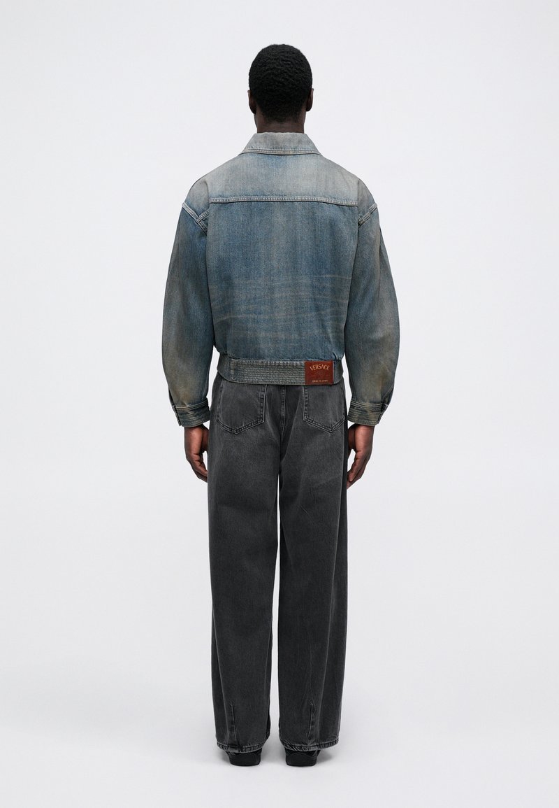 Jeansjacke in Lichtwäsche mit einer Rückenpasse, kombiniert mit locker sitzenden grauen Jeans. Auffälliges markiertes Lederetikett am Bund.