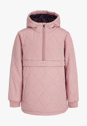 Personne portant une veste matelassée rose et un pantalon noir avec des taches blanches abstraites, assortis à des bottes d'hiver noires.