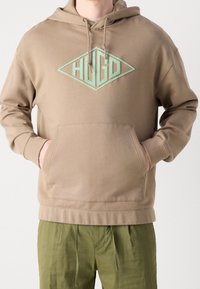Felpa con cappuccio beige con logo ricamato a forma di diamante in verde menta. Presenta una tasca frontale e polsini a coste.