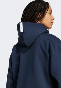 Marineblauwe hoodie met een zachte textuur, oversized pasvorm en een label op de achterkant. Heeft een ronde capuchon en verlaagde schouders.
