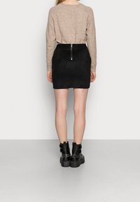 Jupe mini en suède noir avec détail de fermeture éclair au dos, associée à un pull en tricot beige et des bottines noires à semelle épaisse. Texture lisse, design ajusté.