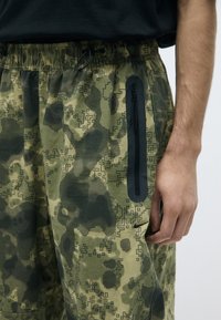 Shorts met camouflagepatroon in tinten groen met zwarte accenten. Voorzien van een elastische taille en een ritssluitingzak aan de zijkant.