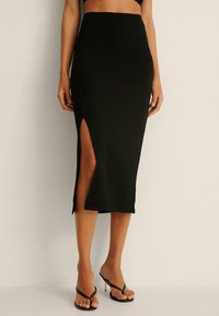 Musta ribbed midi hame, jossa on korkea halkio yhdellä sivulla, teksturoitu kangas ja istuva siluetti. Yhdistetty avonaisen varren kengillä.