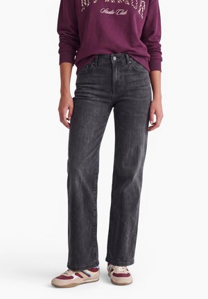 Personne portant un jean noir taille haute droit, un sweat bordeaux avec texte, et des baskets beige et bordeaux avec des bandes bleues.
