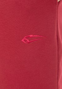 Rode sweatshirtstof met een gladde textuur heeft een klein, geborduurd logo in een contrasterende kleur aan de linkerkant.
