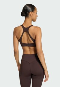 Braletă sportivă maro cu un design tip racerback și spate deschis. Material neted și elastic, cu cusături minime și o formă ajustată.