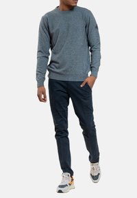 Maglione grigio a maglia con scollo rotondo, abbinato a pantaloni blu scuro e sneakers multicolore. Texture liscia, vestibilità casual e design semplice.