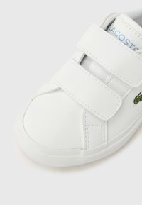 Λευκό συνθετικό αθλητικό παπούτσι με δύο ιμάντες τύπου hook-and-loop, στρογγυλεμένη μύτη, υφασμένο πέλμα και πράσινο κεντητό λογότυπο στην πλευρά.