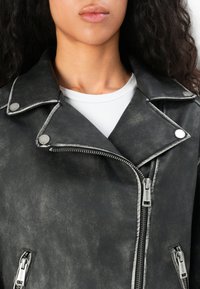 Black faux leather motorcycle jacket with silver hardware, double zip closure, snap buttons, and contrasting stitching details.