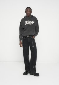 Halli kapuutsiga dressipluus valge graafilise mustriga, kombineeritud mustade laiade pükstega, millel on rhinestone'idega detailid. Väga paksud mustad platvormkingad täiendavad välimust.