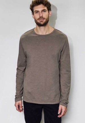 Olijfgroene katoenen shirt met lange mouwen en een ronde hals, voorzien van een klein logo op de borst en een gestructureerde stof. Draagt met donkere broek.