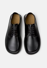 Schwarze Lederschuhe mit glatter Oberfläche, gerundetem Zeh und acht Ösen-Schnürung; strukturierte Innensohle sichtbar.