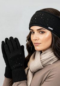 Zwarte gebreide handschoenen met geribbelde boorden, voorzien van kleine glinsterende accenten. Een bijpassende zwarte hoofdband en een beige sjaal maken de look compleet.