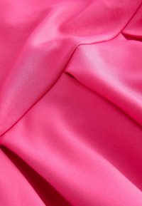 Tissu lisse et rose vif avec des plis doux et une texture subtile, capturant la lumière et l'ombre lors d'une vue rapprochée du matériau.