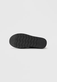 Svart gummisul med ett zigzag-mönster; platt, rund klack; texturerad yta för grepp; minimalistic design.