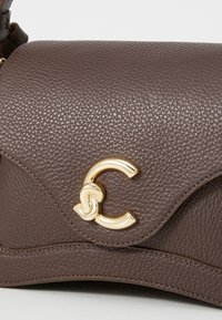 Sac à main en cuir marron avec une finition texturée, une quincaillerie dorée et un design de rabat incurvé distinctif mettant en avant un accent doré en forme de lettre "C".