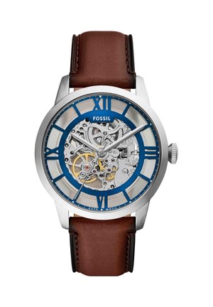 Orologio da polso Fossil in argento con cinturino in pelle marrone, numeri romani blu e ingranaggi meccanici interni visibili attraverso il quadrante trasparente.