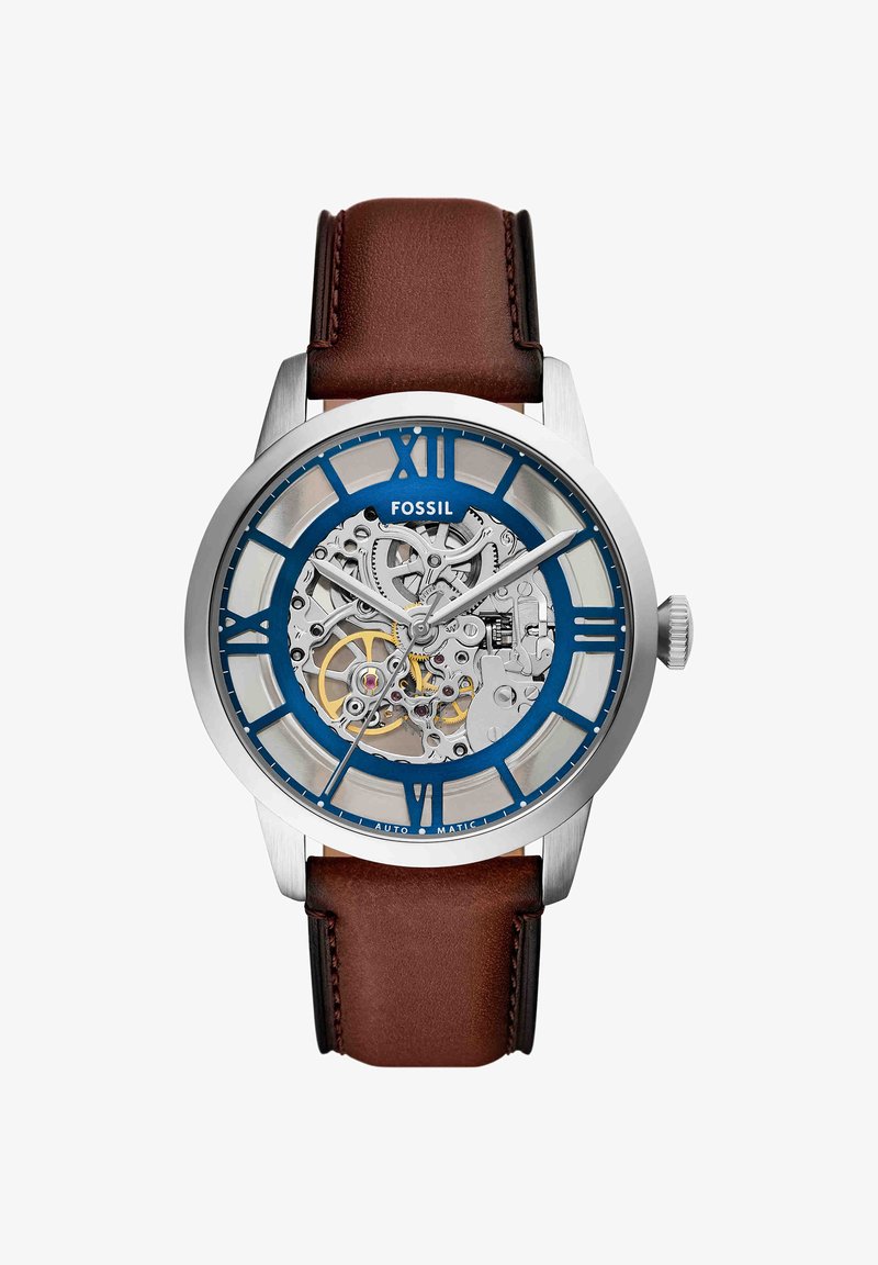 Montre-bracelet Fossil en argent avec bracelet en cuir marron, chiffres romains bleus et engrenages mécaniques internes visibles à travers un cadran transparent.