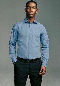 Helles blaues Langarmhemd mit Button-down-Kragen, Knöpfen auf der Vorderseite und glatter Textur, kombiniert mit schwarzen Hosen.