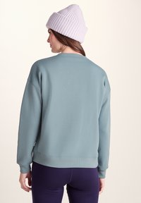 Light blue oversized sweatshirt with a ribbed neckline and cuffs, paired with dark purple leggings and a light purple ribbed beanie.