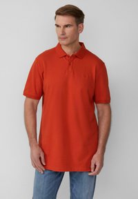 Rotes Polohemd mit Kragen und zwei Knöpfen, aus Baumwollmaterial. Besitzt kurze Ärmel und einen geraden Saum. Wird mit blauen Jeans getragen.
