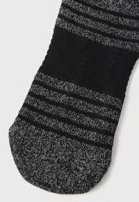 Svart og grå sokk med et strukturert strikkemønster, med tynne horisontale striper. Glatt fotbunn og strukturert kant for god passform.