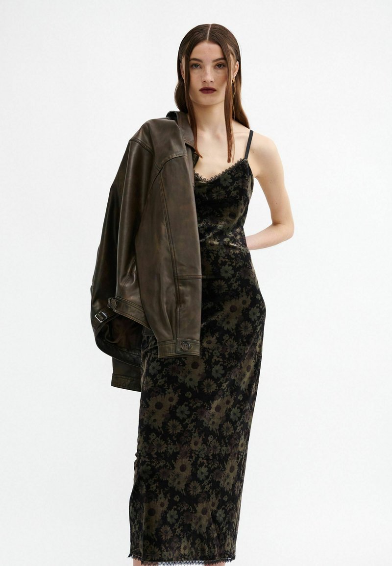Schwarzes Blumenkleid mit satinierter Oberfläche, verziert mit feinem Spitzenbesatz, kombiniert mit einer braunen Lederjacke. Das Outfit verfügt über verstellbare Träger.