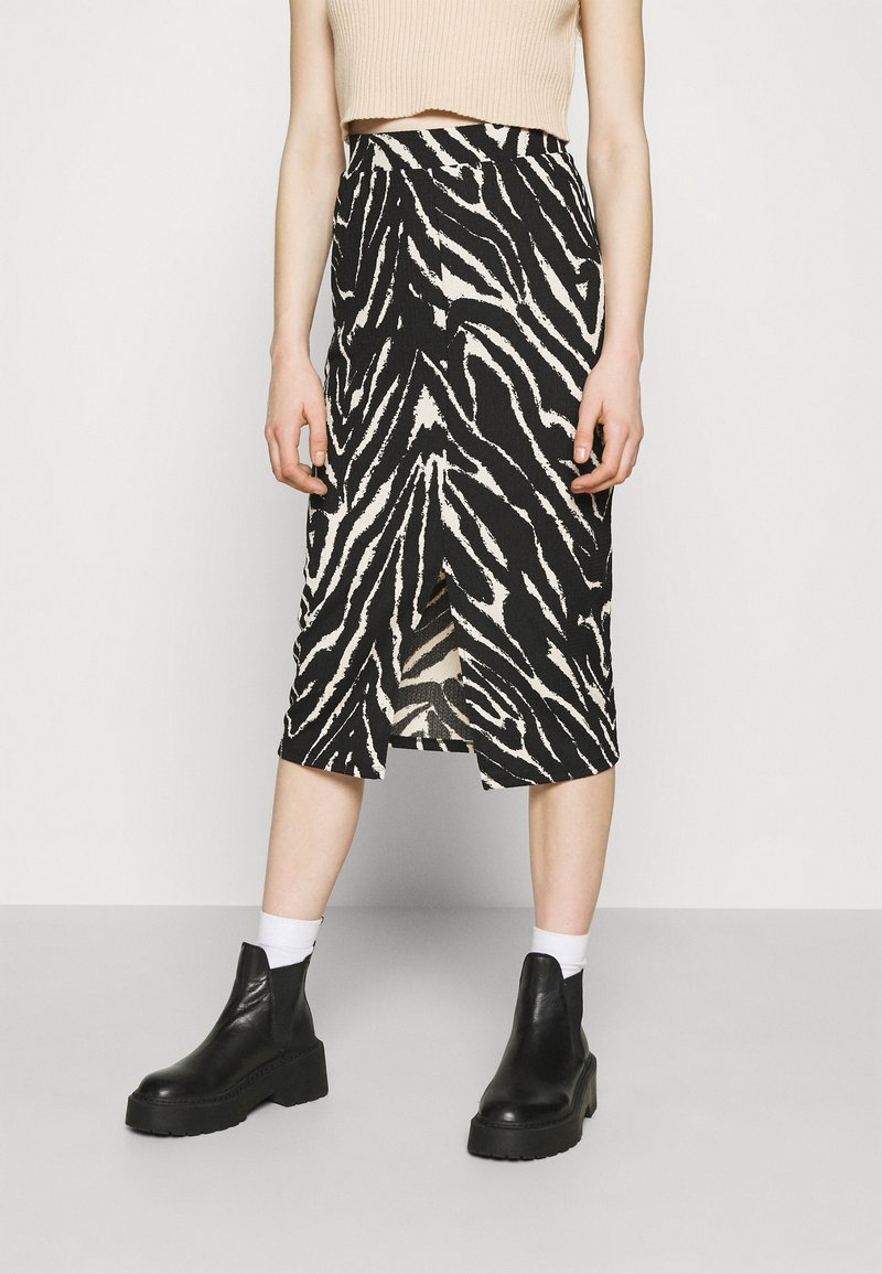 Personne portant un crop top beige sans manches, une jupe midi zèbre noire et blanche, des chaussettes blanches et des bottines noires, debout à l'intérieur.