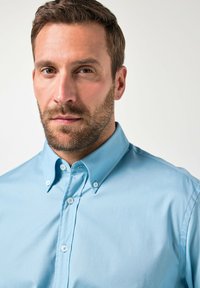 Camisa de botón azul claro con cuello extendido, que presenta una textura suave y un brillo sutil, complementada con botones blancos.