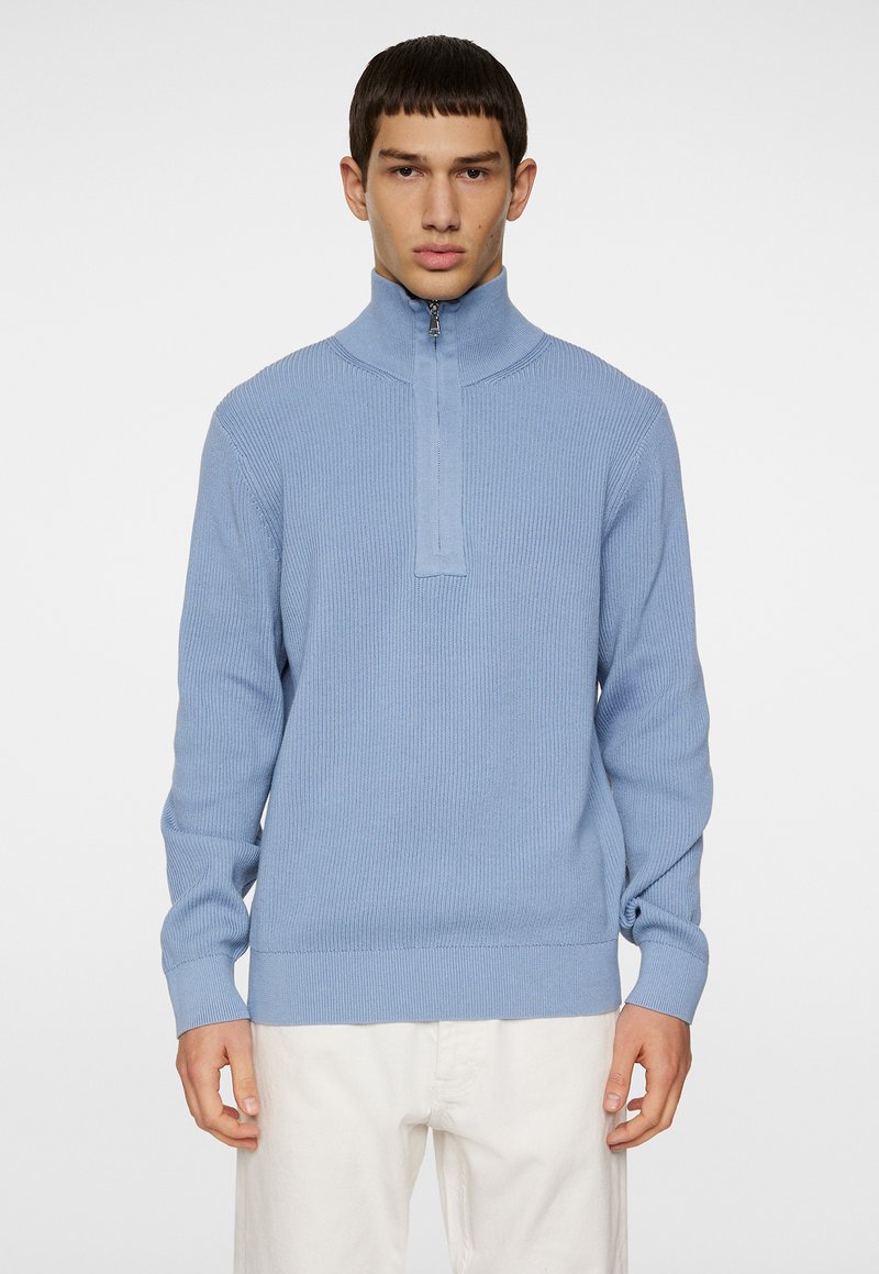 Hellblauer gerippter Pullover mit einem Halbreißverschlusskragen, langen Ärmeln und strukturierter Stoffqualität. Figurbetontes Design in einfarbiger Ausführung mit minimalen Details.