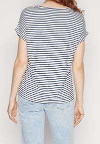 Pruhované tričko v námořnické modré a bílé barvě, s volným střihem, ohrnutými krátkými rukávy a kulatým výstřihem. V kombinaci se světle modrými džínami.