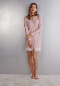Ljust rosa nattlinne med långa ärmar, spetsdetaljer vid fållen och ärmsluten, knappstängning fram och en avslappnad passform.