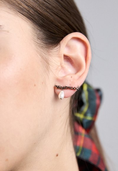 Melna metāla auskari ar vārdu "Westwood", papildināti ar asaru formas balto pērli. Izskatās ar gludu apdari un mūsdienīgu dizainu.