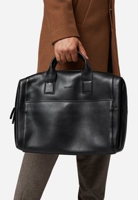 Schwarze Lederhandtasche mit zwei oberen Griffen, glatter Textur, rechteckiger Form und einer Fronttasche. Markenlogo auf der Vorderseite sichtbar.