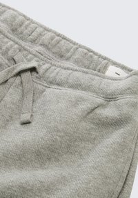 Szare dresowe spodnie o miękkiej, teksturowanej tkaninie. Posiadają elastyczny pas z sznurkiem oraz subtelne metaliczne drobinki rozmieszczone na całej powierzchni.