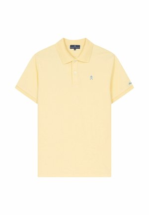 Polo de manga corta de color amarillo pálido con cuello, tapeta de dos botones, pequeño logo azul de palos de golf cruzados en el lado izquierdo del pecho y bordado en la manga.
