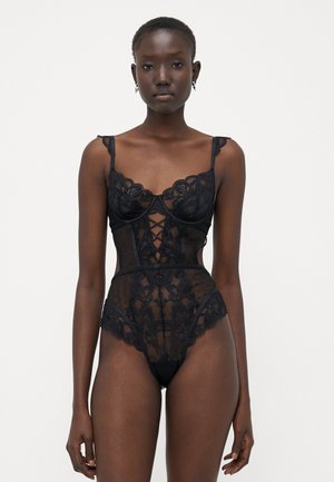 Body din dantelă neagră, cu modele florale, panouri transparente, bretele ajustabile și un detaliu frontal în cruce, având un croi înalt al picioarelor.