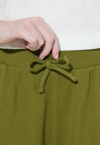 Olijfgroene textuurshorts met een striksluiting in de taille. De stof heeft een fijn ruitpatroon, wat zorgt voor een ontspannen, ademende pasvorm.