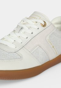 Άσπρα και μπεζ αθλητικά παπούτσια Tommy Hilfiger με λευκά κορδόνια, υφασμένες πλευρικές επιφάνειες, χρυσή τρύπα κορδονιού και καφέ λαστιχένια σόλα.